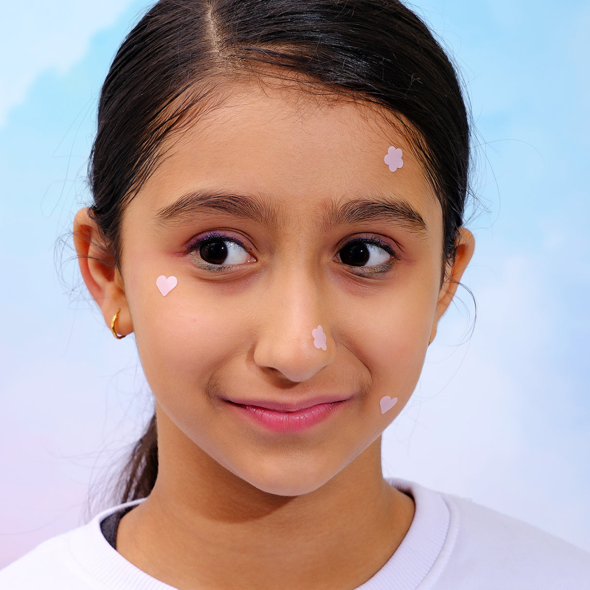 Young girl with heart-shaped stickers on her face against a light blue background