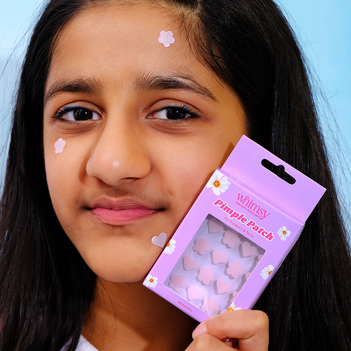 Girl holding a purple package of pimple patches with a blue background