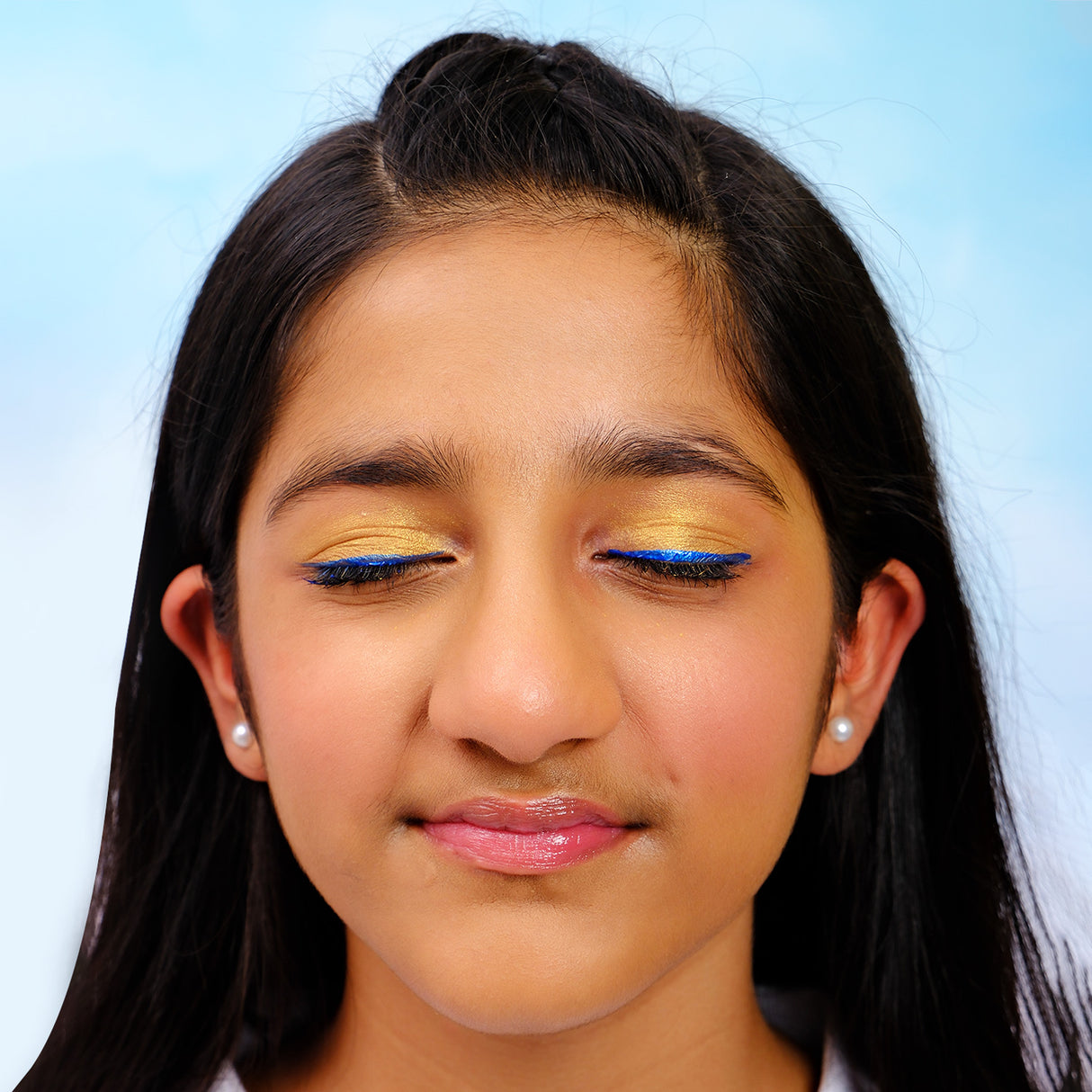 Close-up of a girl with blue eyeliner and pink lipstick against a light blue background