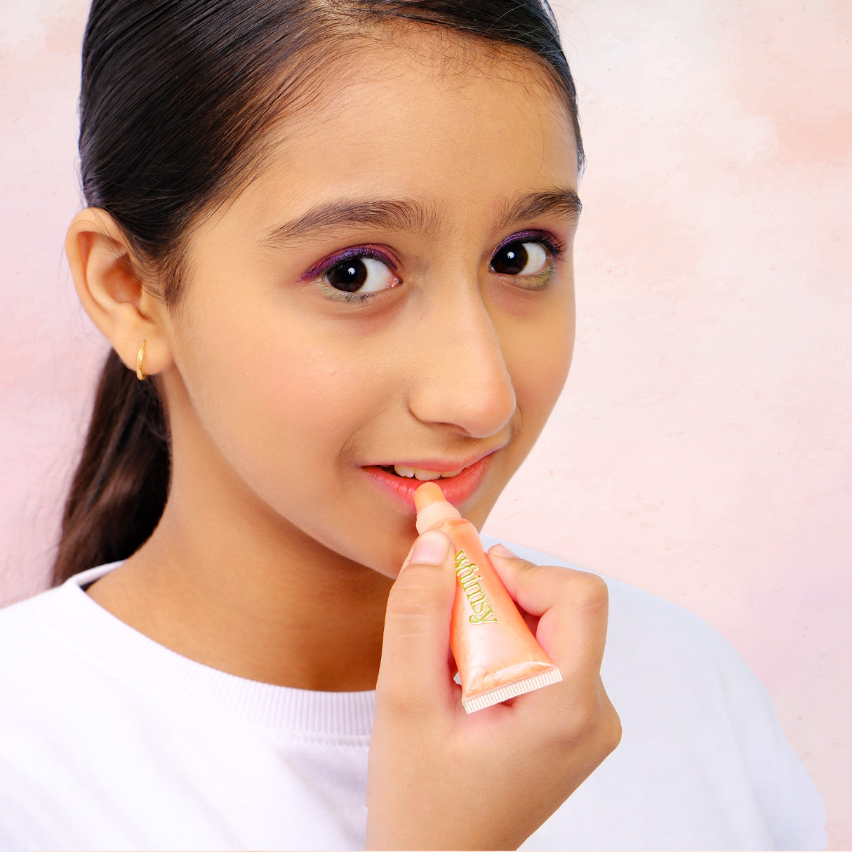 Person applying lip balm to their lips with a pink background