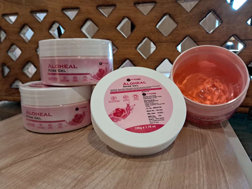 Aloheal Rose Gel containers on a wooden surface with a wooden chair in the background.