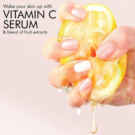Hand holding a sliced lemon with text about vitamin C serum and fruit extracts on a light pink background