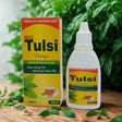 MG Tulsi Drops packaging and bottle on a wooden surface with green leaves in the background