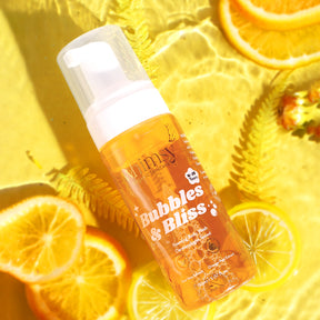 whimsy Bubbles & Bliss bottle on a yellow background with orange slices