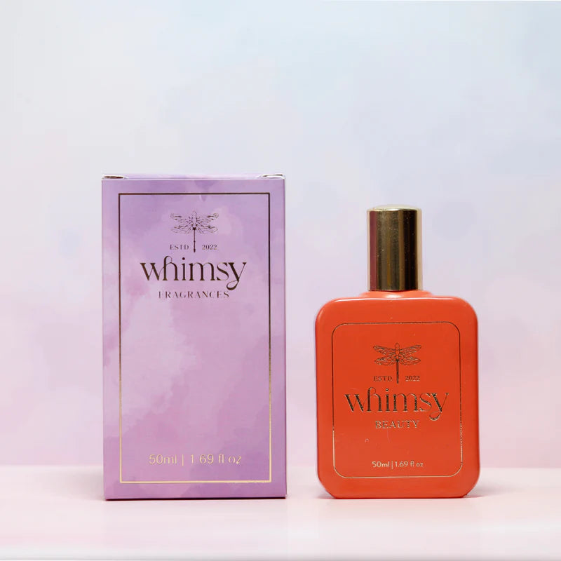 Orange perfume bottle and purple packaging with 'whimsy' branding on a light pink background